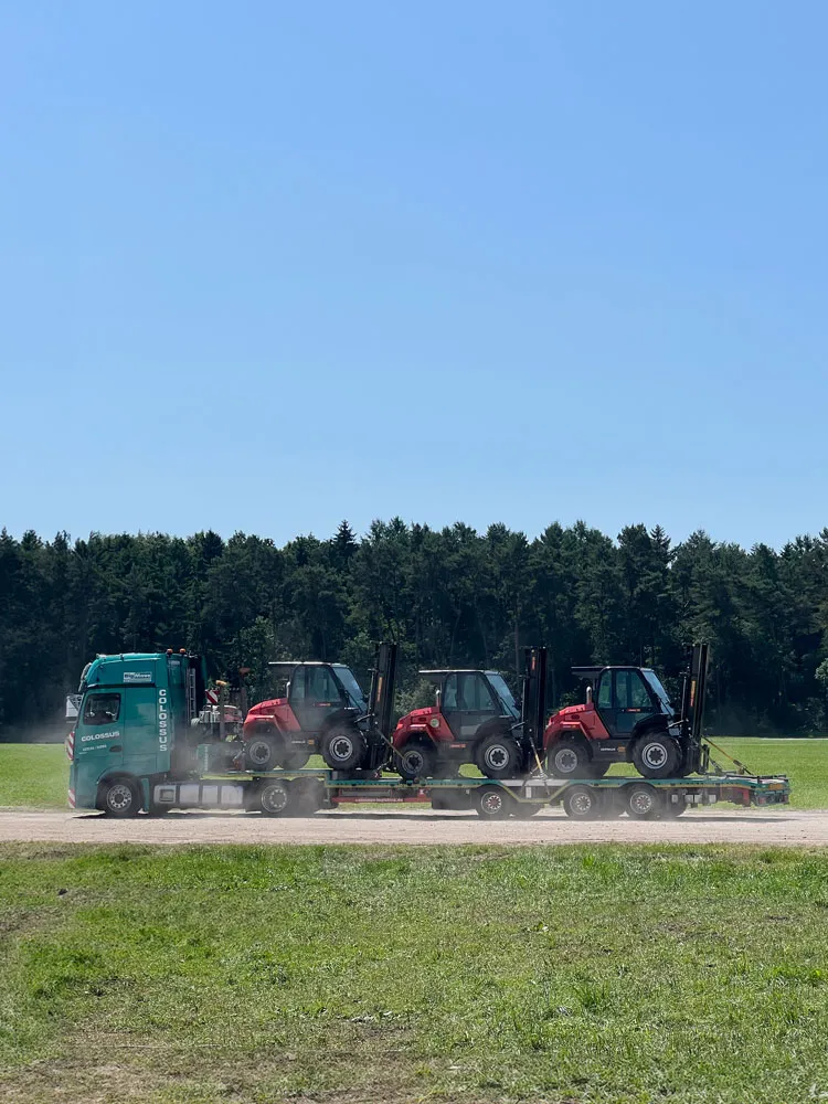 Lkw transportiert drei Geländestapler an einem Waldrand entlang