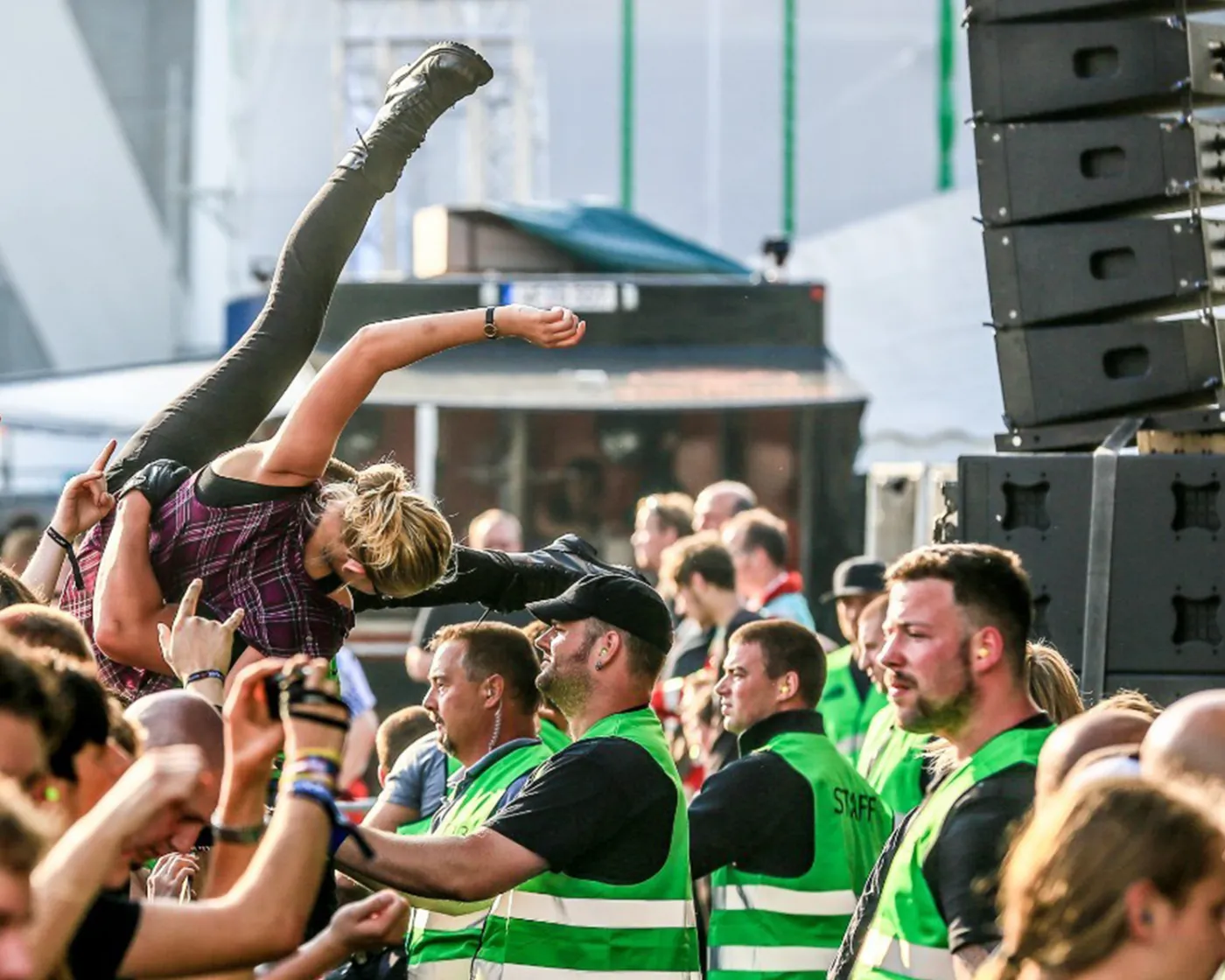 Ordnungsdienst in grünen Westen vor der Bühne, darüber ein Crowdsurfer