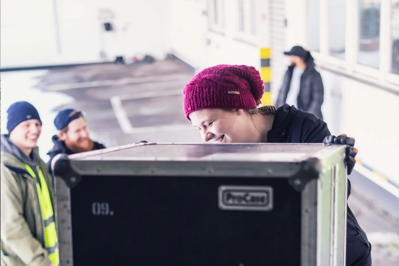 Crew-Mitglied mit roter Mütze bewegt ein Flightcase, daneben zwei Kollegen