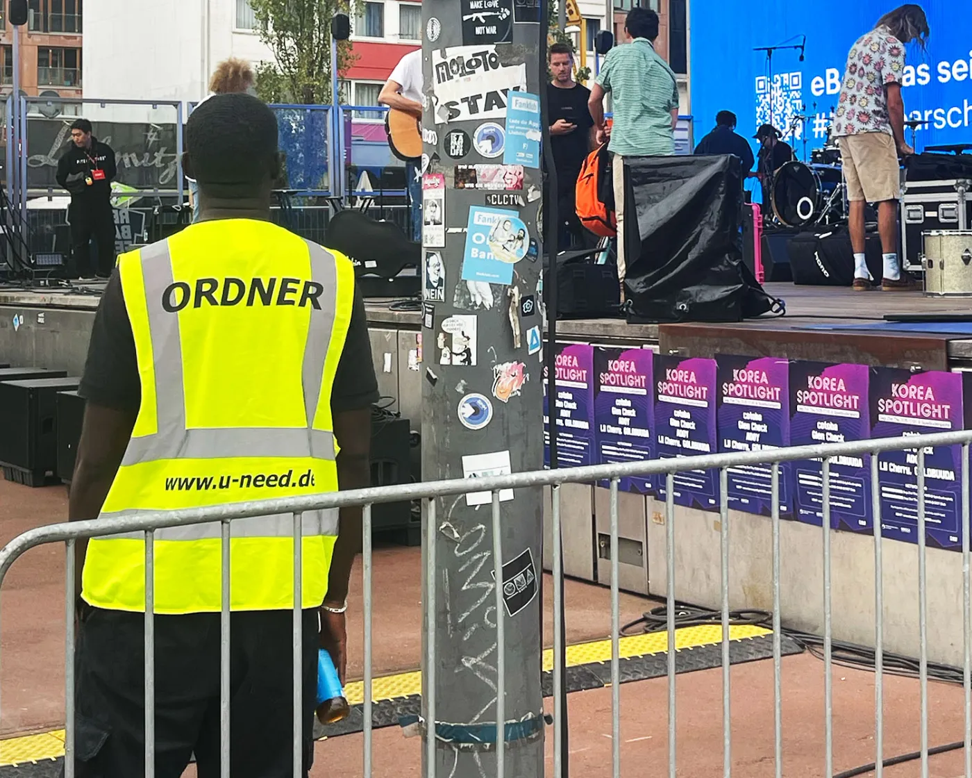 Ordner in gelber U-Need-Weste an der Absperrung vor einer Bühne
